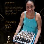 Mulher de pele clara e cabelos escuros presos, sorrindo enquanto segura um tabuleiro adaptado de xadrez para deficientes visuais. Ela veste uma blusa azul-turquesa sem mangas e está posicionada diante de um fundo preto com detalhes dourados. Ao lado da imagem, há um depoimento sobre sua primeira aula de xadrez utilizando um tabuleiro emprestado pela MXDV. Em destaque, aparece a frase: “Inclusão salva vidas!”. No canto inferior esquerdo, está o logotipo da MXDV – Mulheres enxadristas DV do Brasil